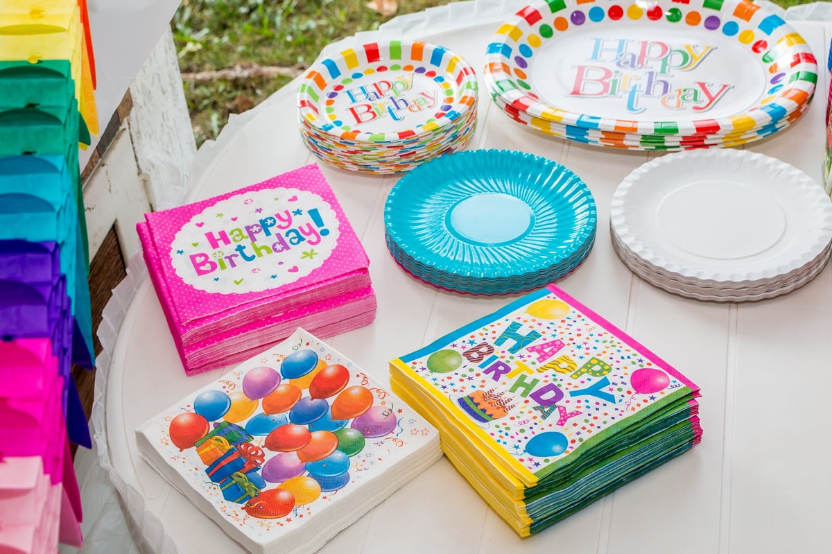 White table served with disposable tableware, colorful napkins and paper plates, ready for birthday party