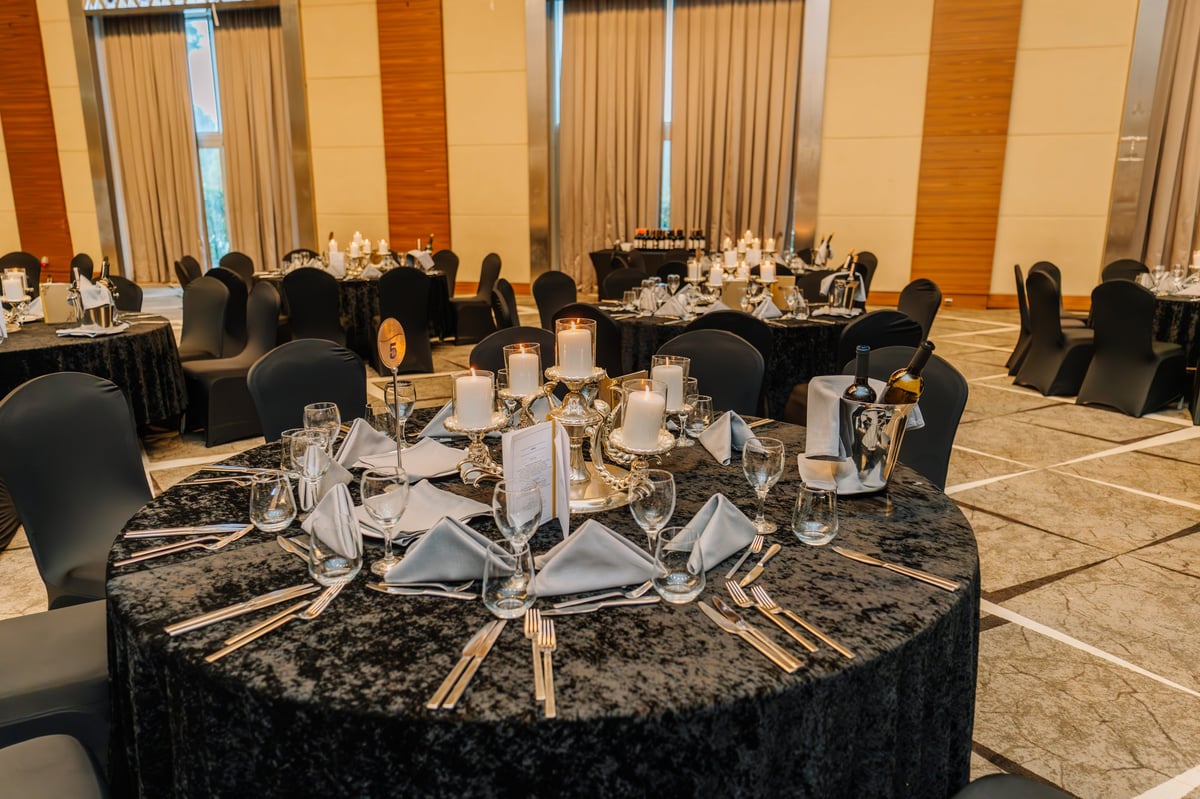 Luxurious banquet hall setup with round tables, candle centerpieces, wine bottles, and elegant place settings prepared for a formal dinner event