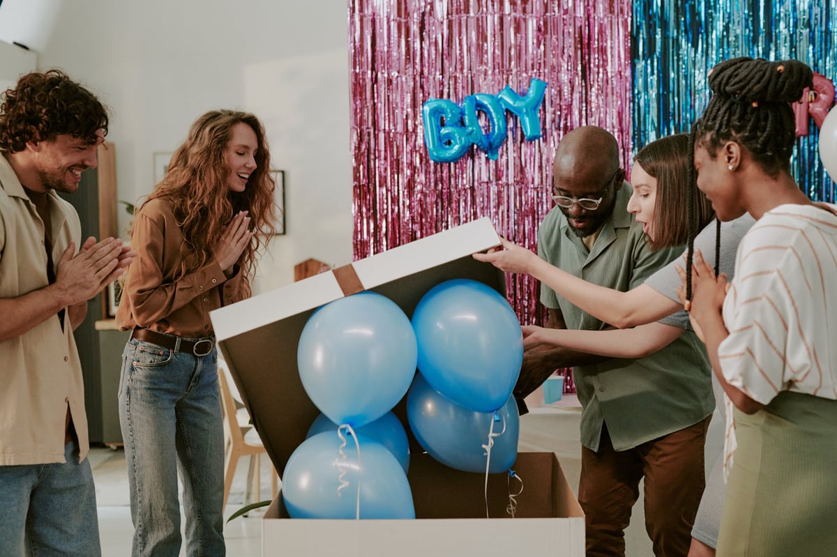 Group opening large box with blue balloons at gender reveal party celebrating together